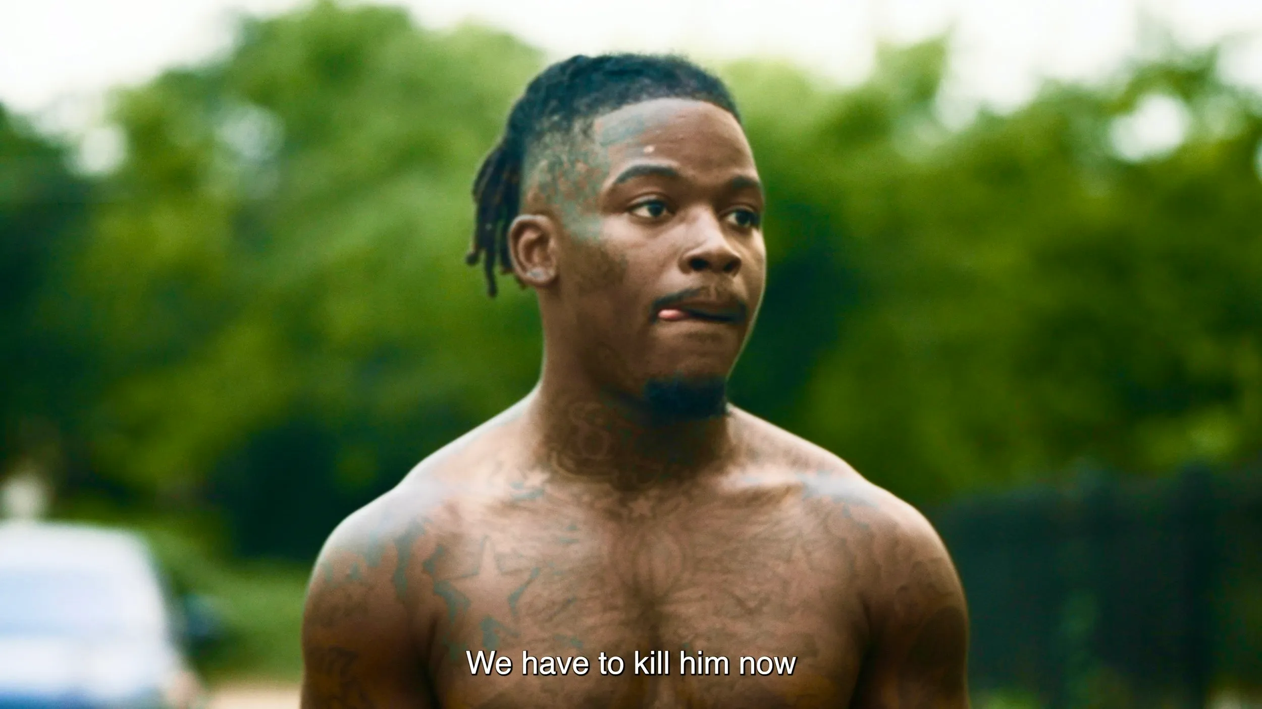 Shirtless young man outdoors on a summer day, subtitled “We have to kill him now”.