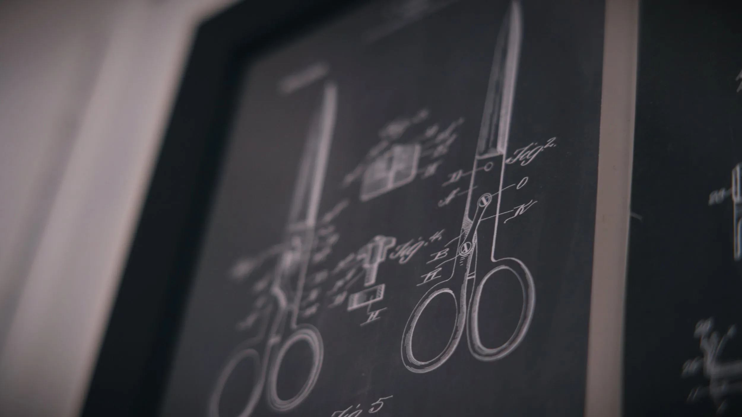 Shallow-focus detail of a framed vintage scissors patent drawing on a salon wall.