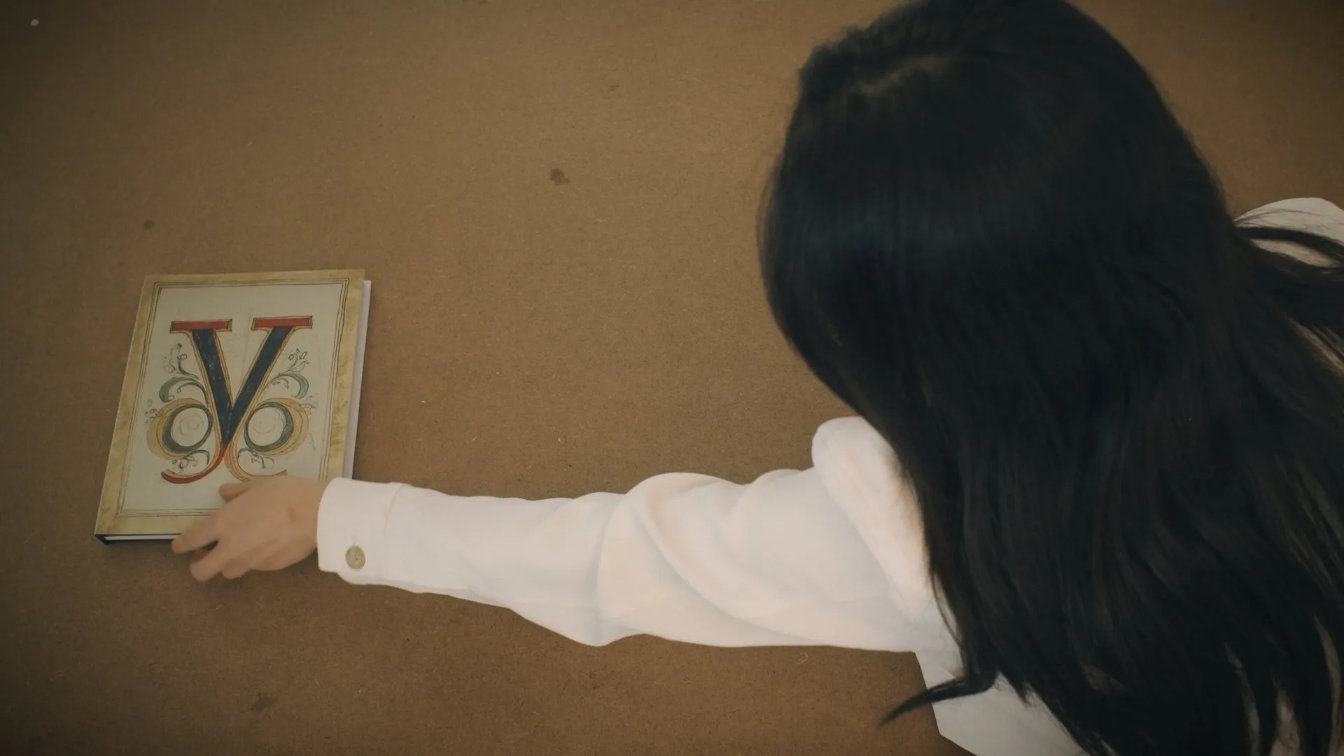 Hand placing an ornate printed letter V on a wooden table.
